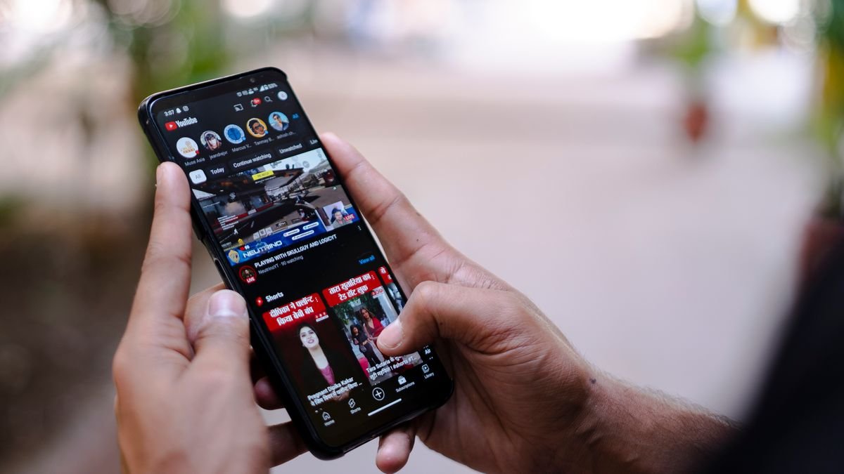 Hands holding a smartphone outdoors with YouTube open