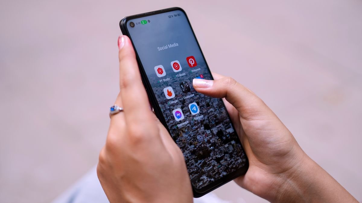 Hands holding a smartphone with a folder of social media apps open