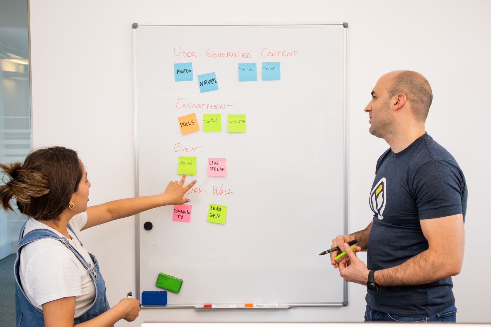Two colleagues planning content on a whiteboard with sticky notes